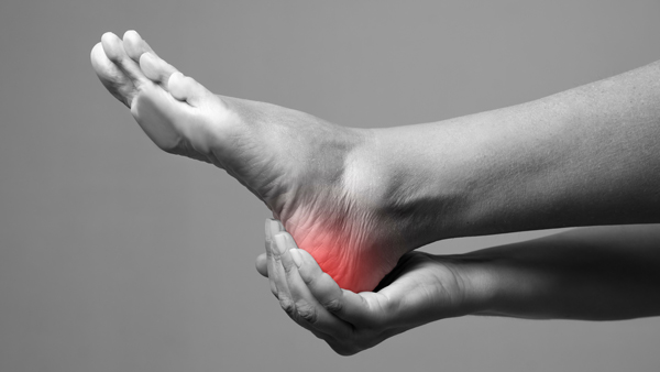 black and white photo of hand holding foot and red highlighted heel pain